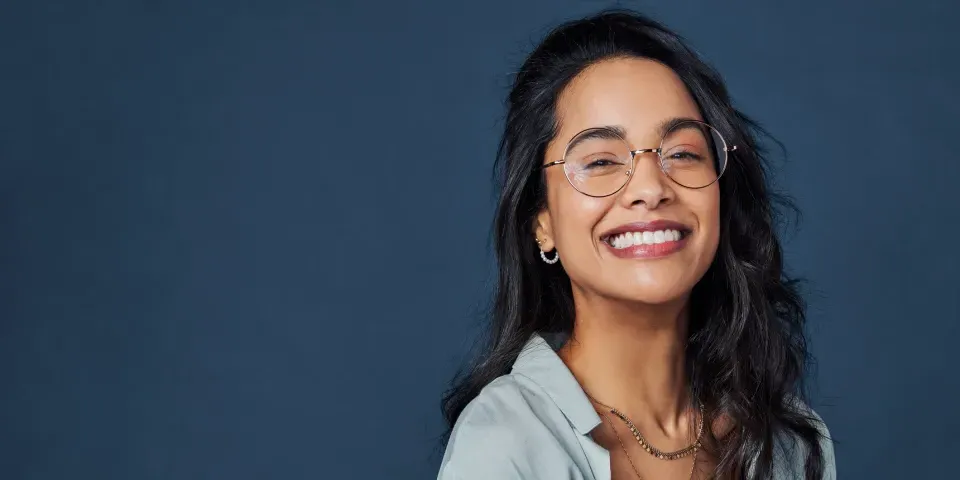 Beautiful university student having fun isolated against blue wall while wearing specs.